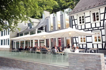 Seminar and conference hotel Große Ledder with outdoor terrace A modern half-timbered house with a terrace full of people sitting under large white umbrellas.