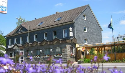 exterior view Traditionele herberg met leistenen gevel, blauwe bloemen op de voorgrond en een zomerse hemel op de achtergrond.