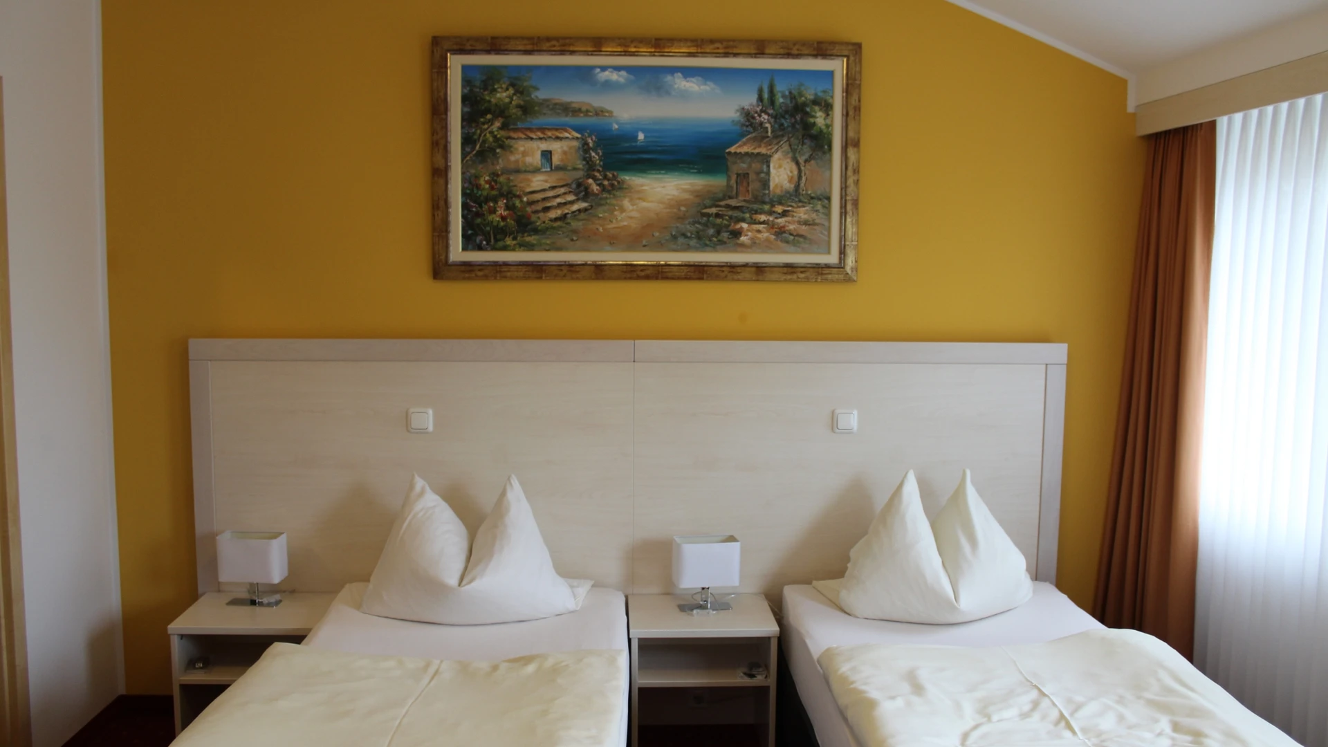Two single beds with white comforters in a room with a yellow-painted wall and coastal image.
