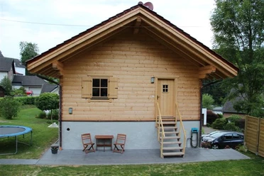 Vakantiehuis Breibach Klein houten huisje met een zadeldak, een klein terras, een tafel en stoelen, omgeven door een groen landschap.