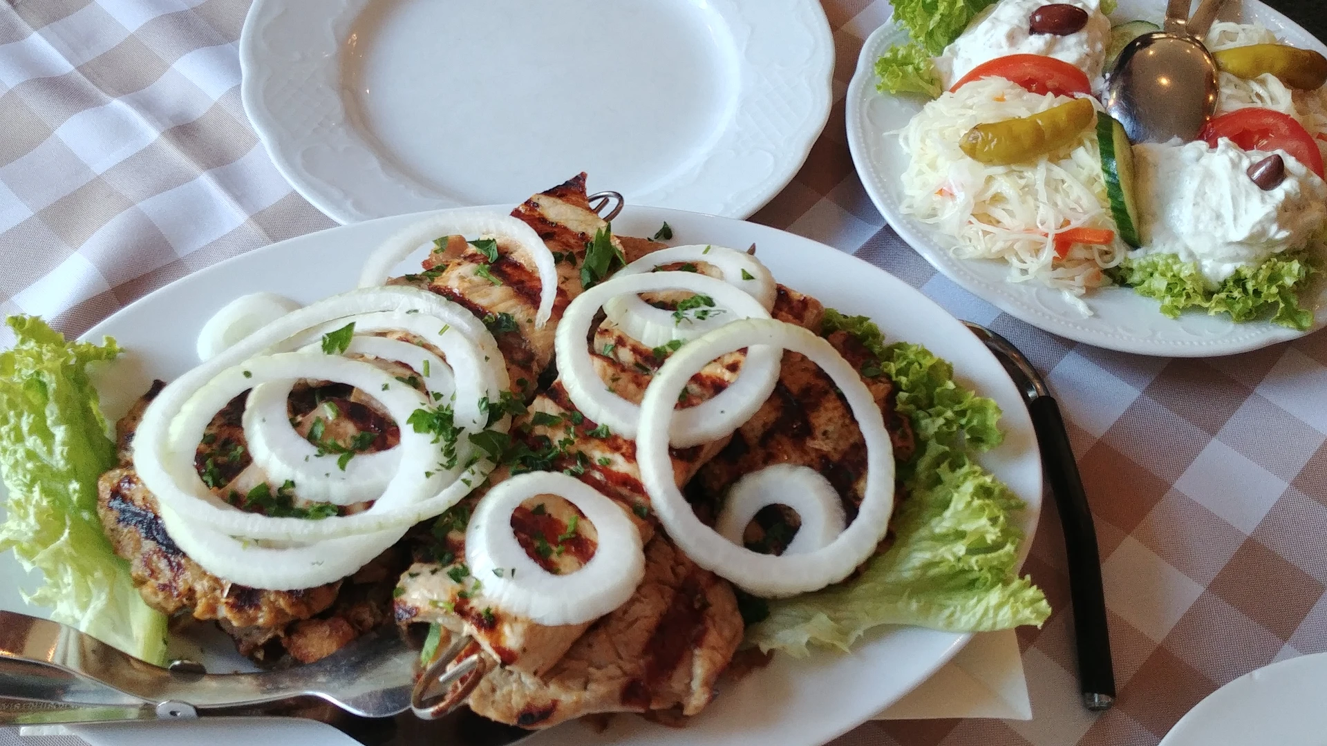 Greek meat platter with grilled meat, fresh onion rings and side salad.