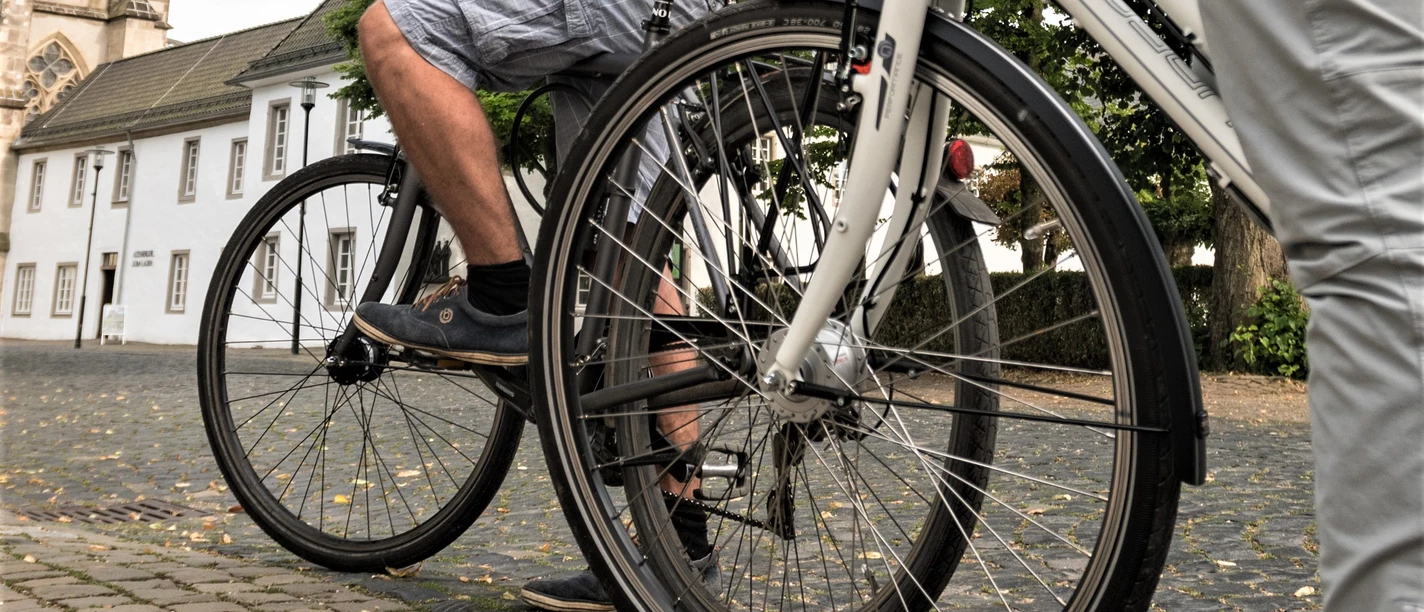 Cycling in Altenberg Two people on bicycles are riding along a paved path in front of a historic building.