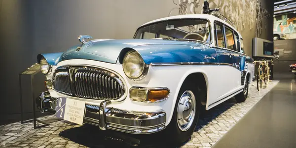 Ein historischer blauer und weißer Oldtimer neben Retro-Fahrrädern in einer Museumsausstellung.