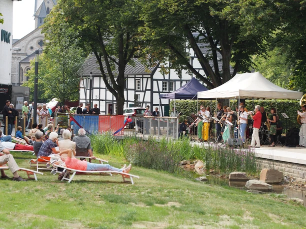 A jazz band is playing on an outdoor stage while spectators relax and listen from deck chairs.