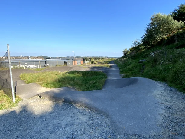 Pumptrack on :metabolon Pumptrack in Lindlar with asphalt hills, surrounded by green meadows and blue sky.