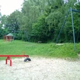 Plac zabaw dla dzieci na Osterholzer Strasse Plac zabaw z czerwoną huśtawką i zjeżdżalnią, otoczony bujną zielenią i zacienionymi drzewami.