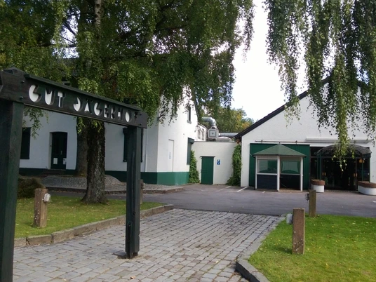 Gut Jägerhof w Erkrath Wejście z łukiem do Gut Jägerhof w Erkrath, otoczone zielenią i utwardzoną ścieżką.