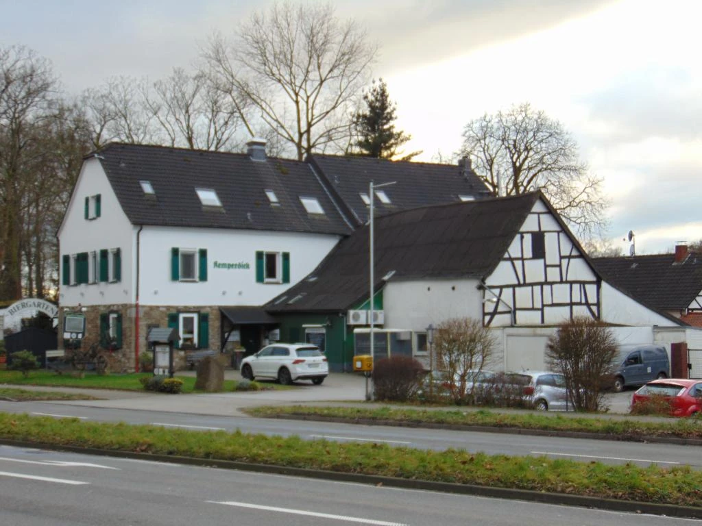 Kemperdick Tradycyjny budynek z muru pruskiego, z drewnianymi okiennicami i przyległym parkingiem przy wiejskiej drodze.