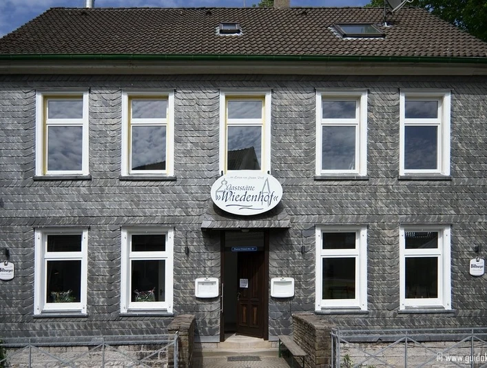 Widok frontowy Palazzo Wiedenhof w Haan Dwupiętrowy budynek z szarą, łupkową fasadą i białymi ramami okiennymi w dzielnicy Haan.