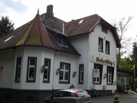 Dom Stolberg Dwupiętrowy dom wiejski z dwuspadowym dachem i oknem dachowym, otoczony drzewami, z zaparkowanymi samochodami przed domem.