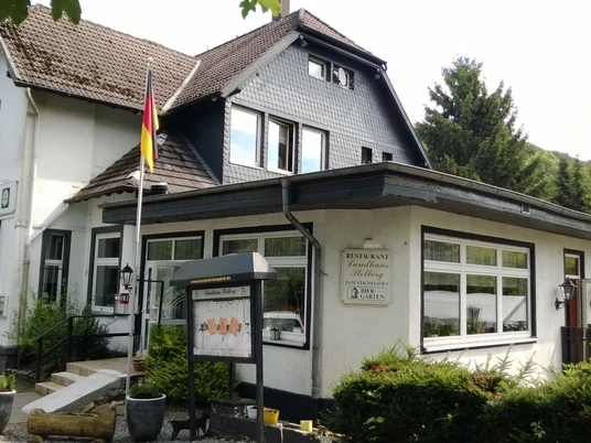 Dom Stolberg Restauracja Landhaus Stolberg z niemiecką flagą, otoczona zielonymi drzewami i widokiem na las.