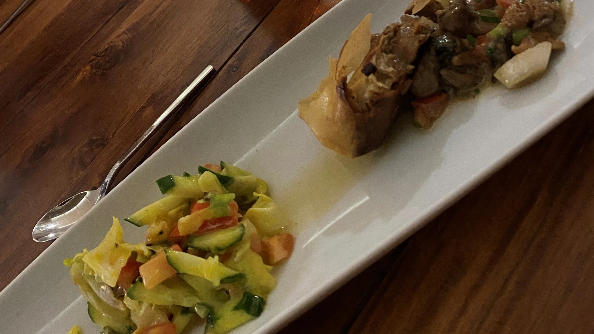 A rectangular plate presents a colorful mix of vegetables and hearty meat rolls on a wooden surface.