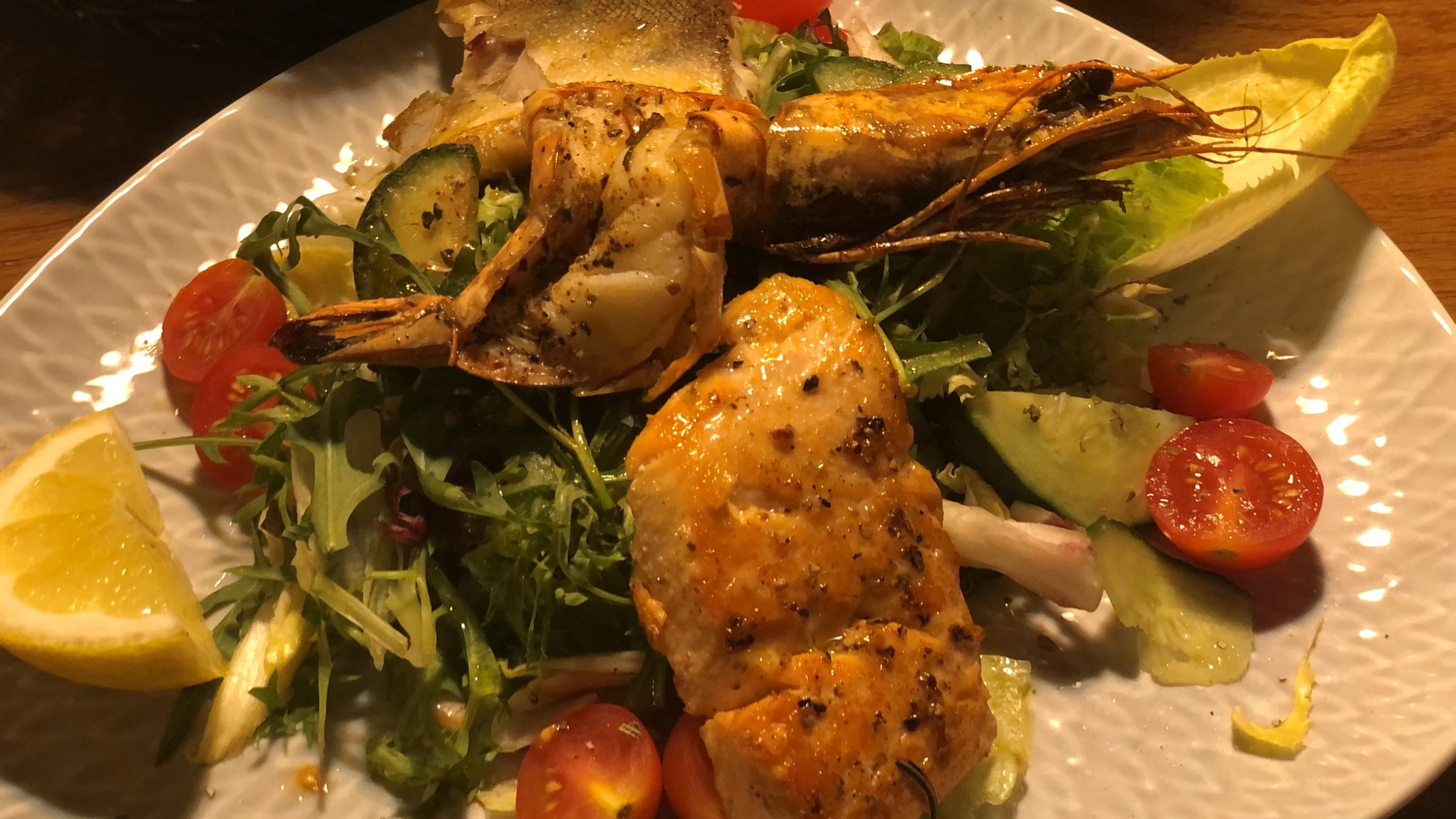 A plate of fried fish, king prawns and a fresh vegetable salad of tomatoes and cucumber.
