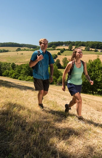 Plaisir de la randonnée dans l'Elfringhauser Suisse Deux personnes marchant sur une colline herbeuse avec de vastes champs et des arbres en arrière-plan.