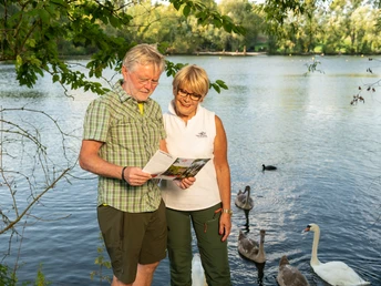 Junto al estanque Abtskücher en Heiligenhaus Una pareja de ancianos se encuentra en la orilla del estanque Abtskücher y examina atentamente un folleto.