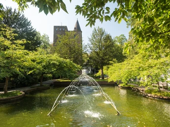 Fontanna zamku Landsberg w pobliżu Ratingen Fontanna z strumieniami wody w parku zamku Landsberg, otoczona zielonymi drzewami.